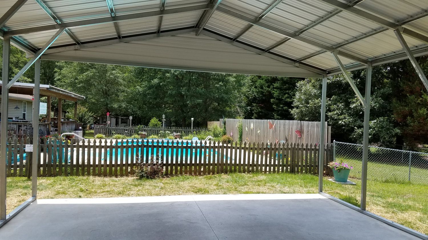 A carport with a fence and a pool in the background.