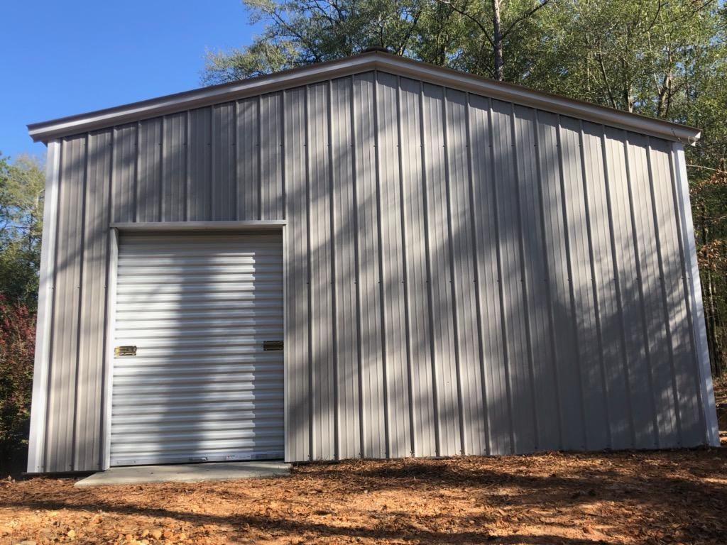A gray metal building with a white garage door is sitting on top of a dirt hill.