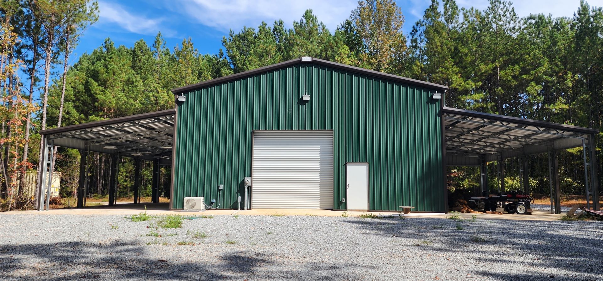 A green building with a white garage door is surrounded by trees.