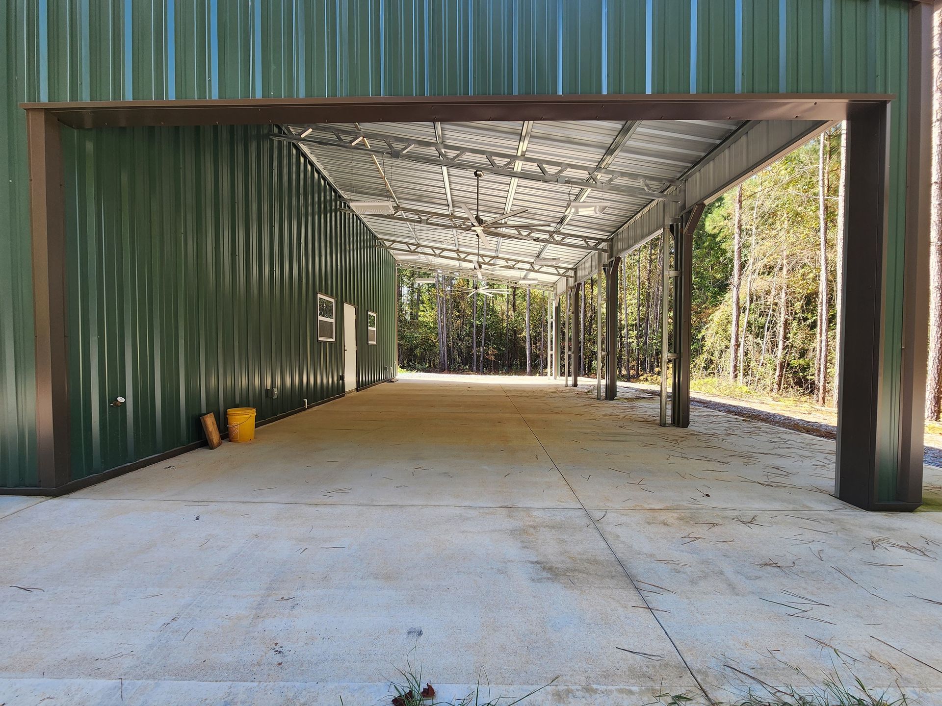 A large green metal building with a concrete driveway underneath it.