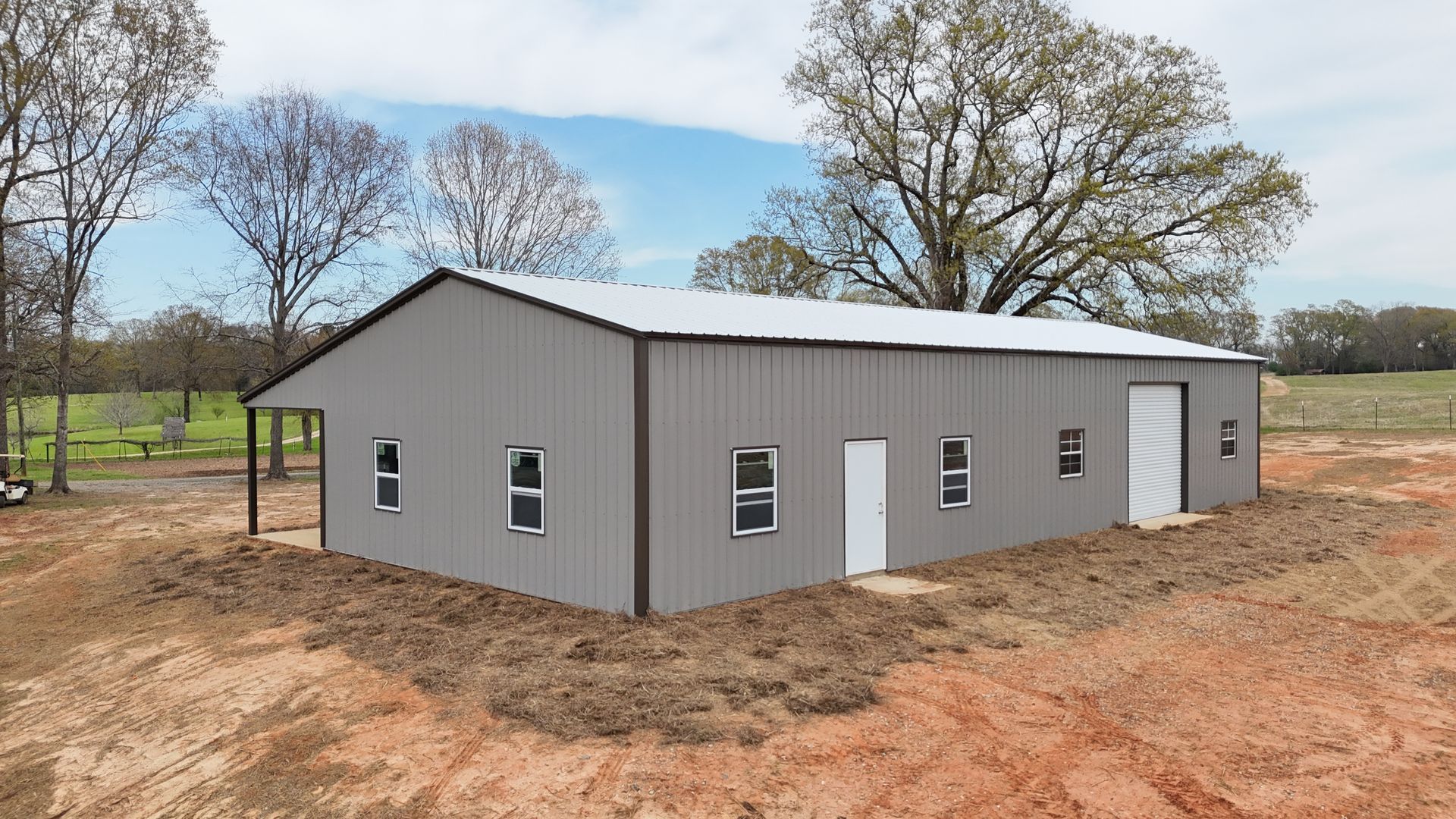 A metal building with three garages and a cover on top of a dirt field