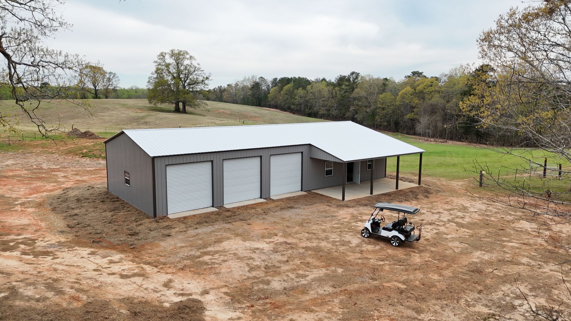A metal building with three garages and a cover on top of a dirt field
