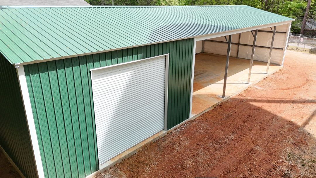 A green and white metal barn is sitting on top of a dirt field.