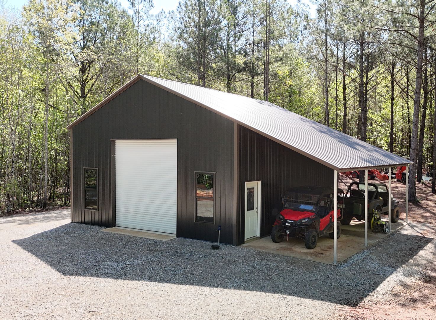 Dark metal building with a carport; a red ATV and utility vehicle are parked nearby.