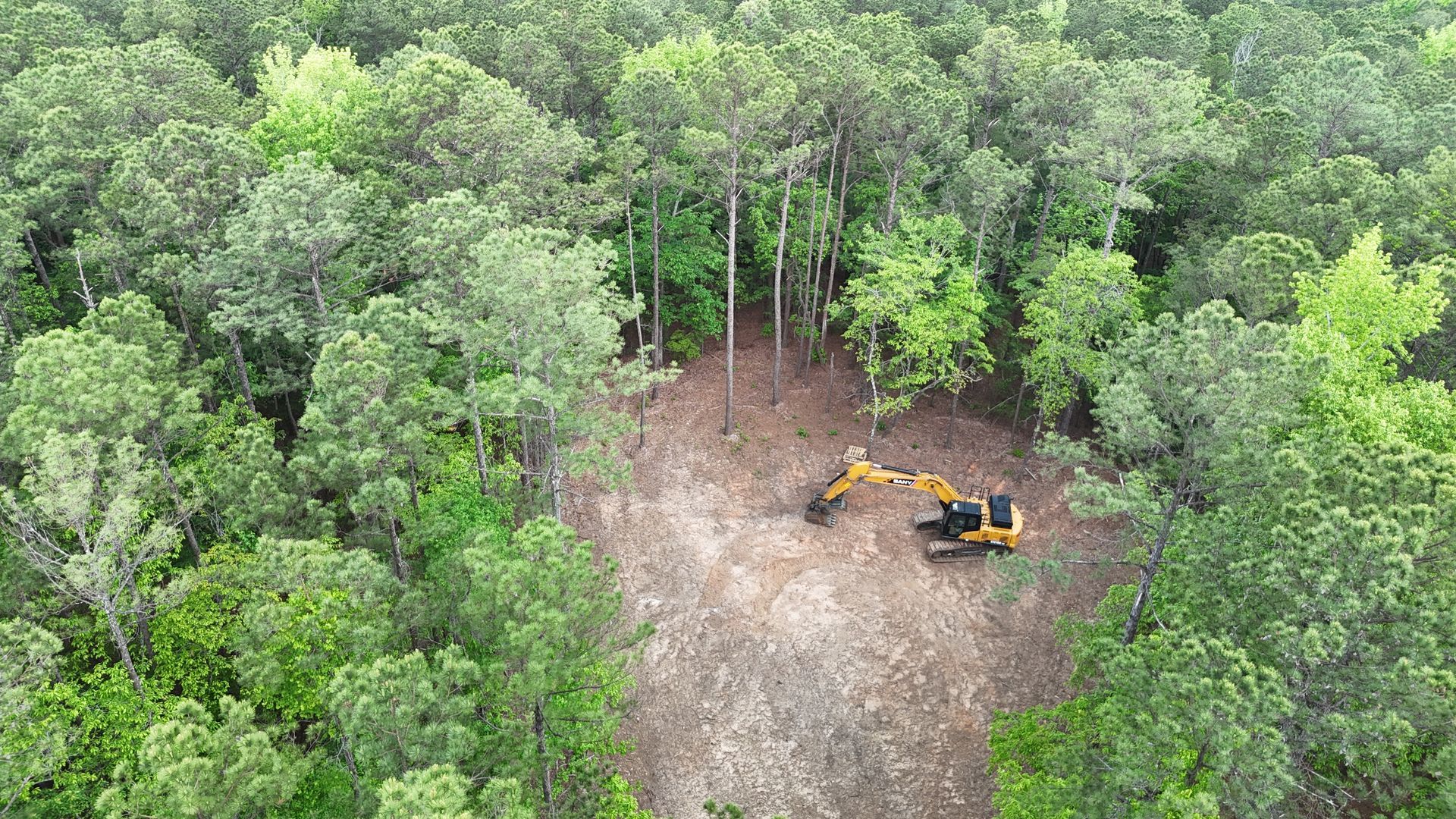 Two excavators clearing a dirt patch in a dense green forest