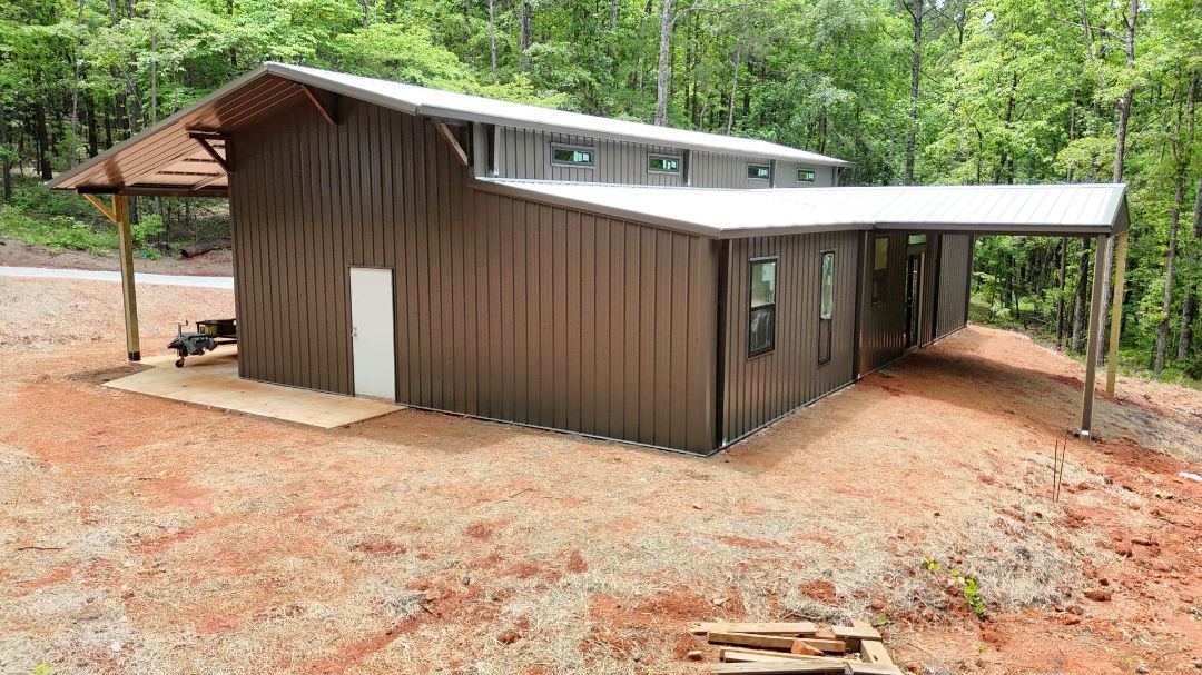 A large metal building with a carport in the woods.