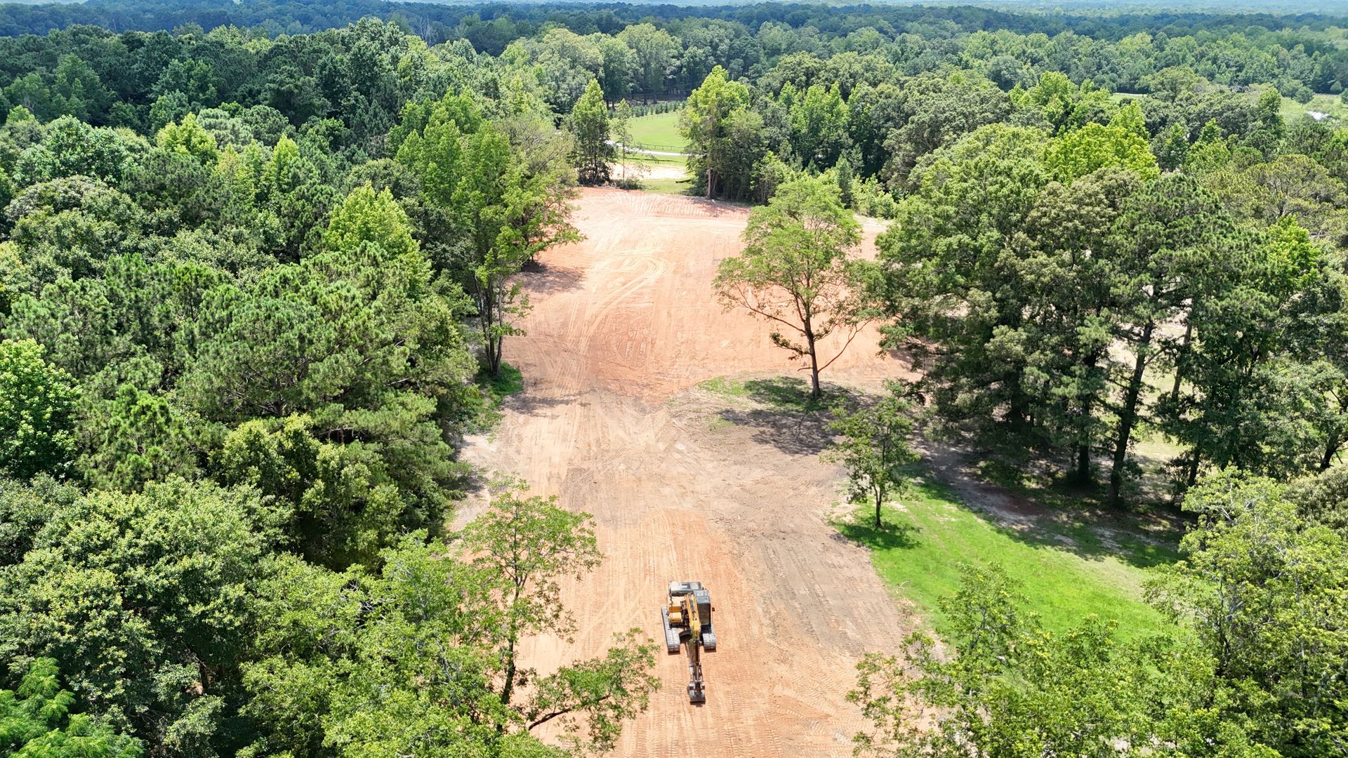 Aerial view of a dirt clearing surrounded by dense green trees, with a lone person walking near the bottom center.