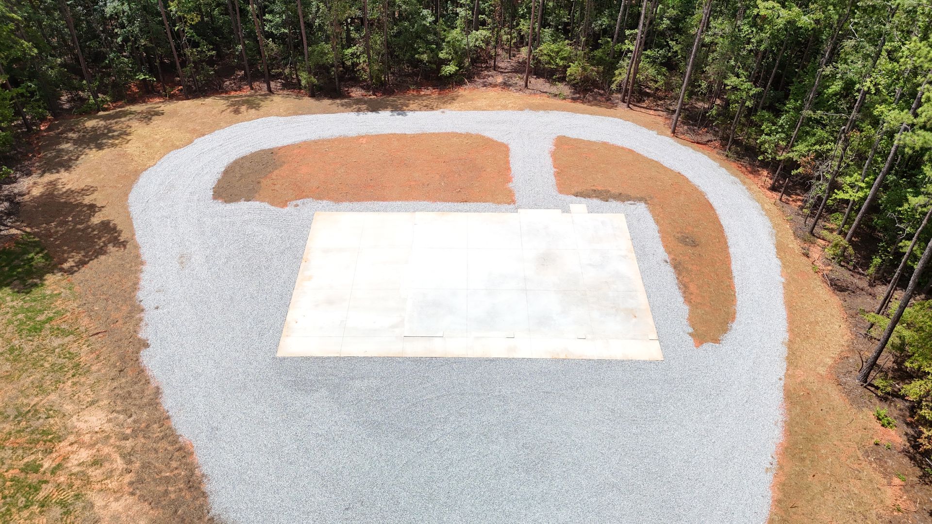 Aerial view of a gravel helipad pad with a white landing marker, surrounded by trees.