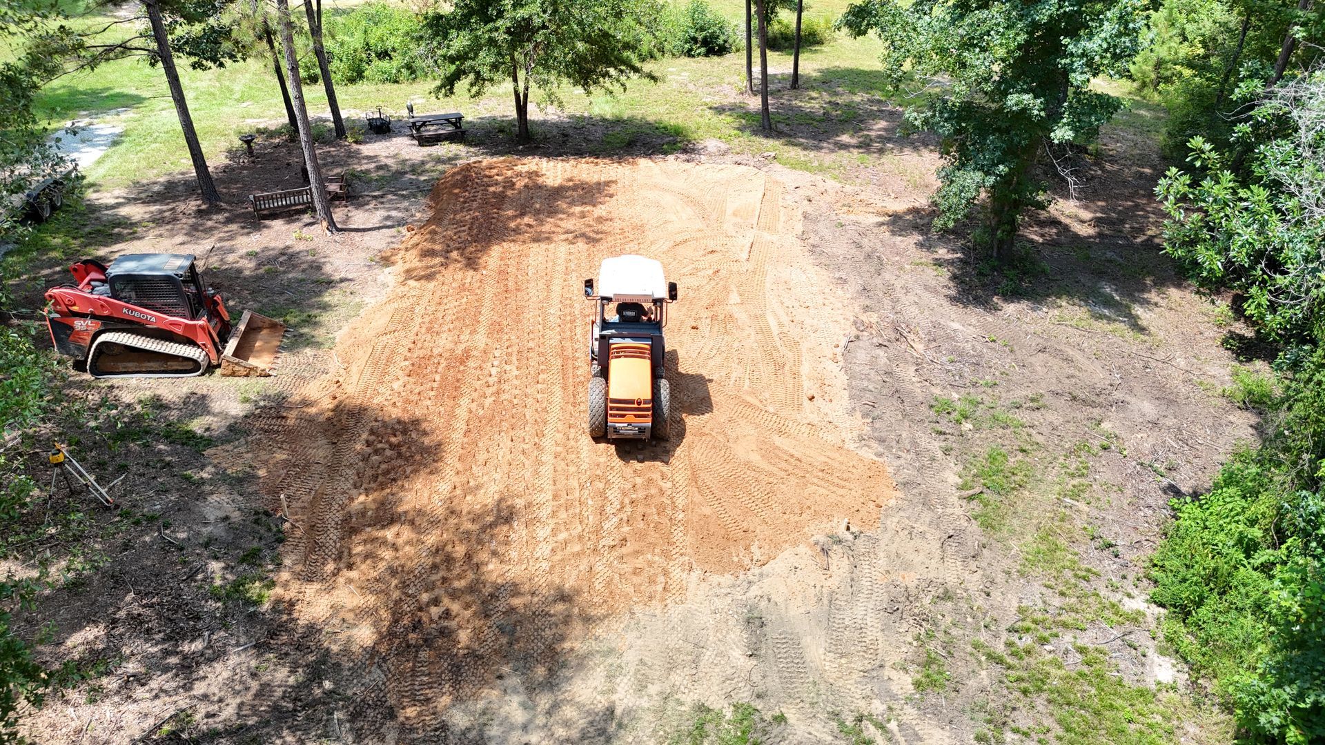 Tractor and small skid steer clearing land surrounded by trees.
