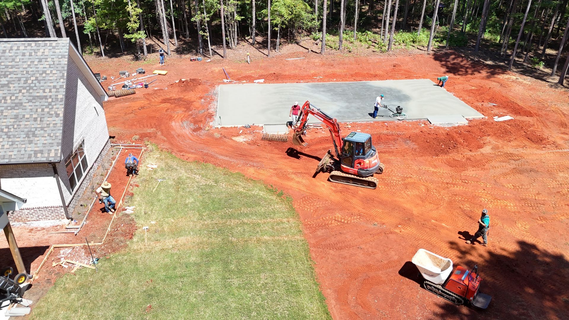 Construction site with an excavator, workers, and a concrete slab foundation.
