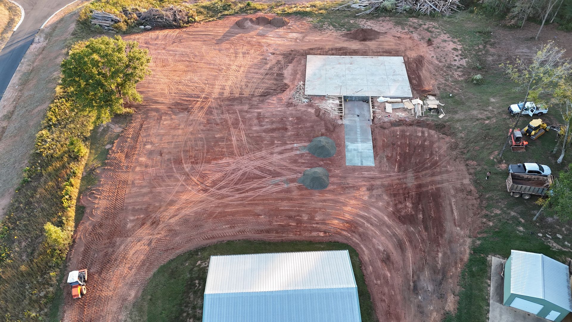 Aerial view of a construction site. Red dirt surrounds a partially built structure and pathway.
