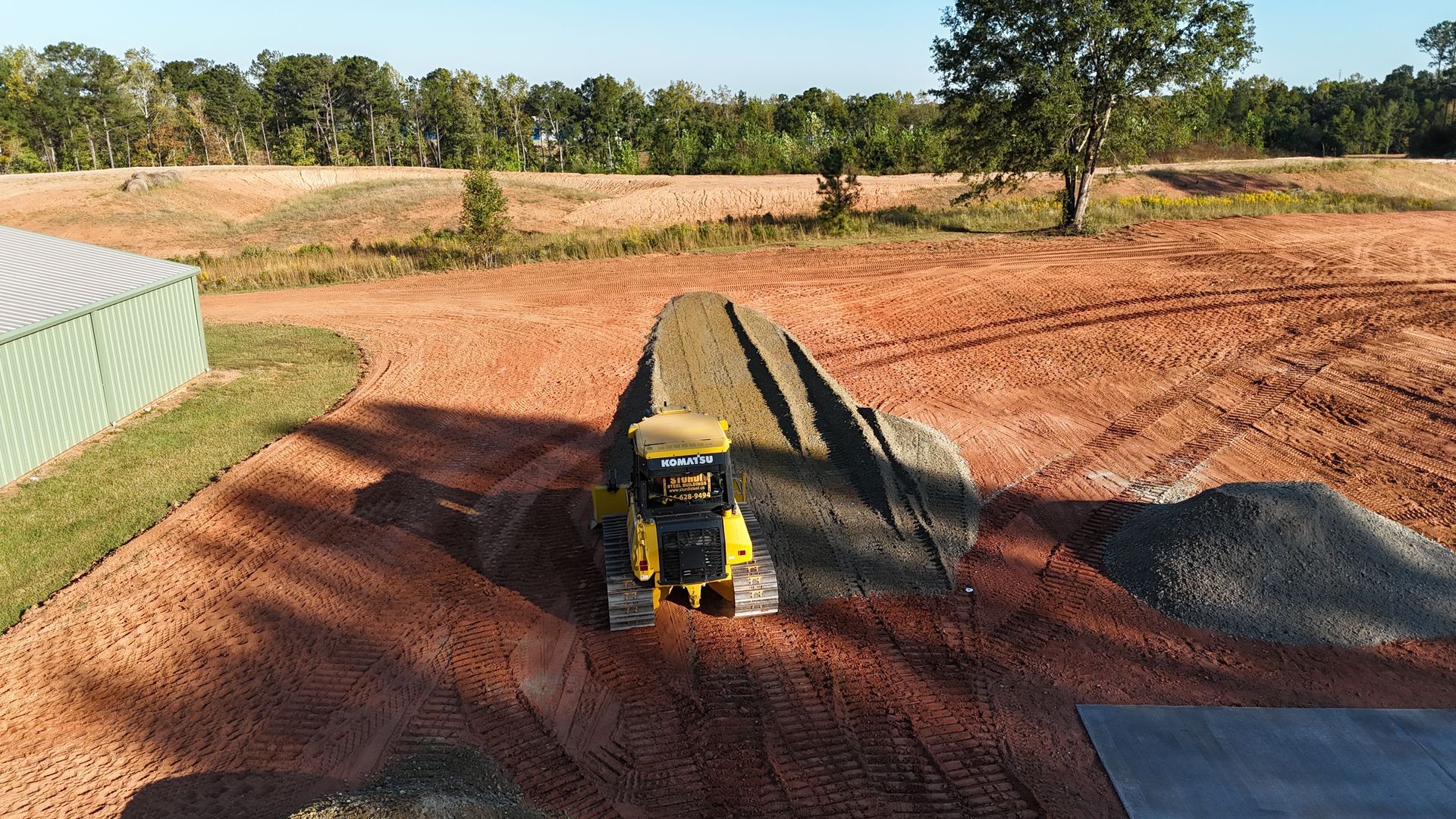 Yellow bulldozer grading dirt in a field; building a berm next to a metal building.