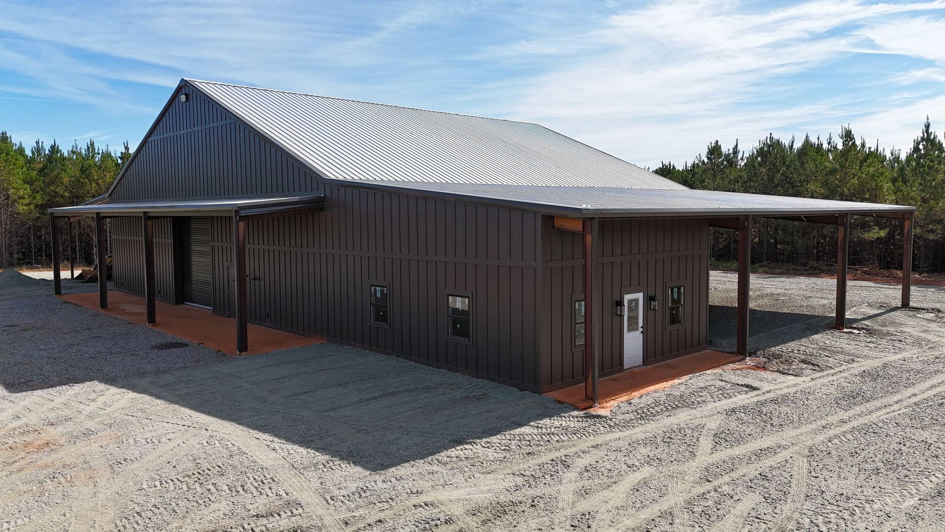 Dark brown metal building with corrugated metal roof and a long porch on a gravel lot.