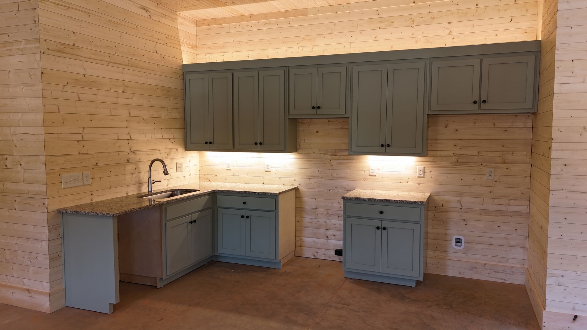Kitchen with pale green cabinets, granite countertops, and light-colored layered walls.