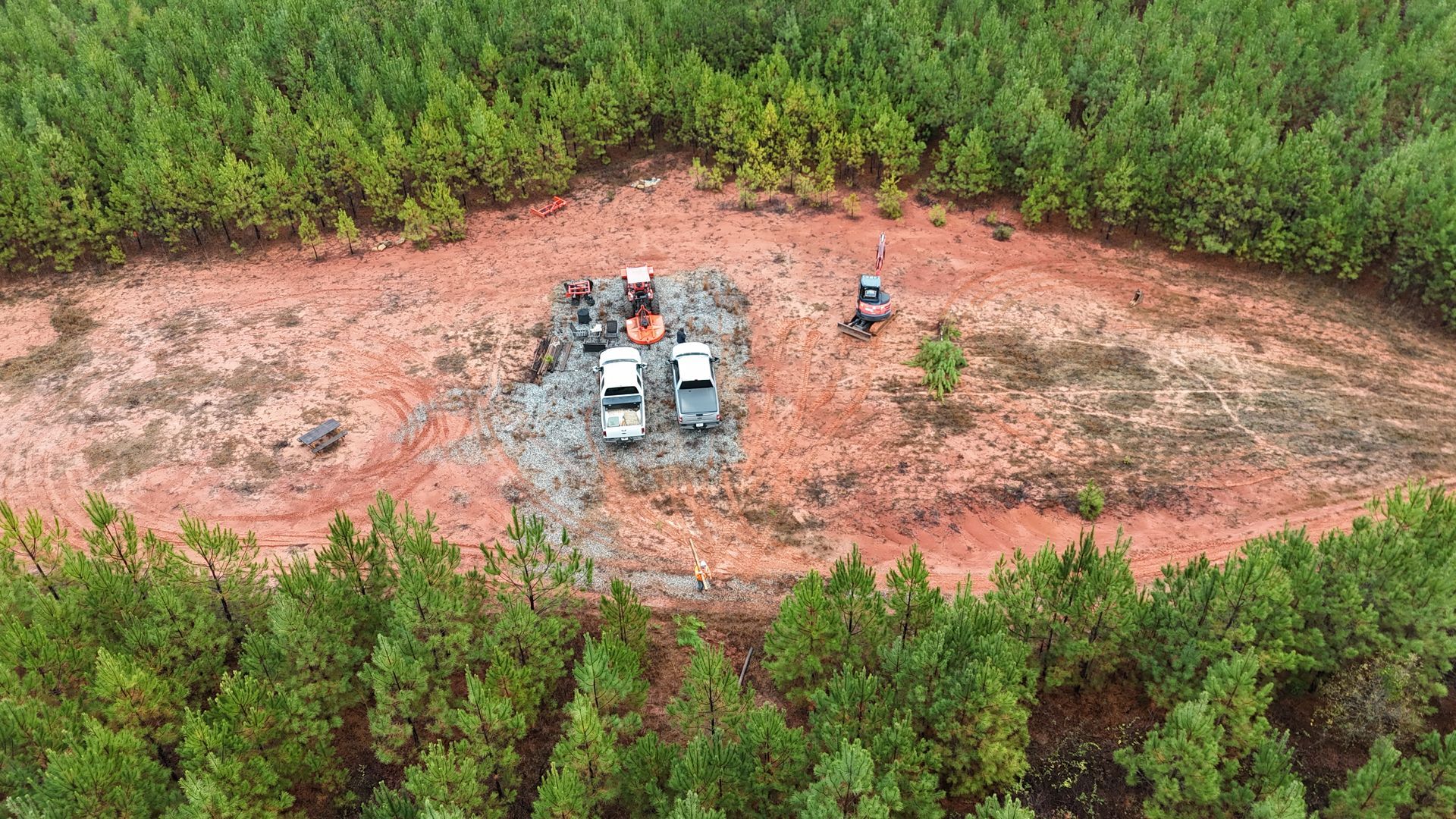 Aerial view of two parked SUVs and people on a cleared dirt patch surrounded by dense green forest