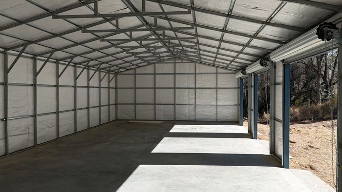 Interior of a metal framed storage building with roll-up doors, concrete floor and white walls.