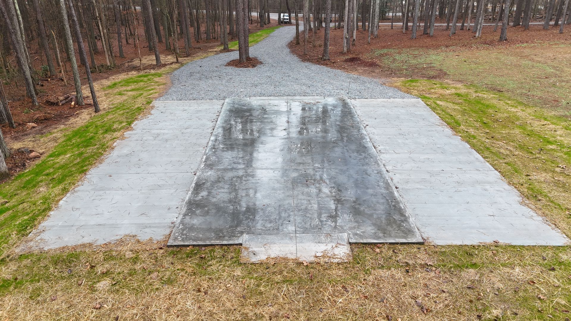 Concrete ramp leading up a wooded trail, flanked by gravel and grass.