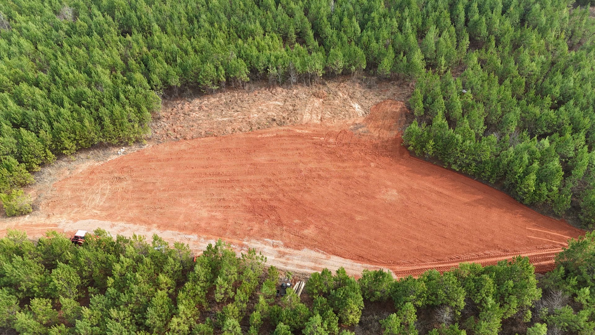 Aerial view of a large reddish-brown cleared patch surrounded by dense green forest.