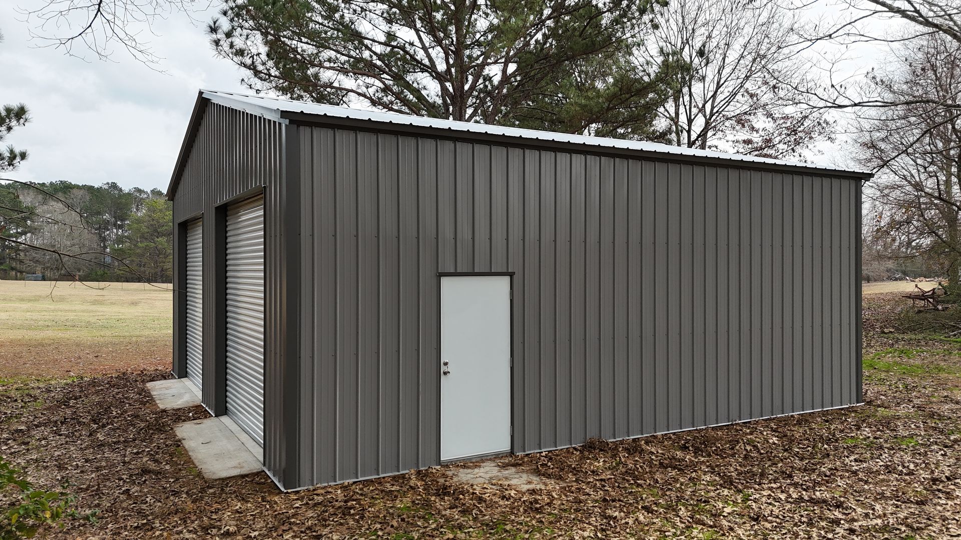 Gray metal shed with two garage doors and a white door, in a grassy area.