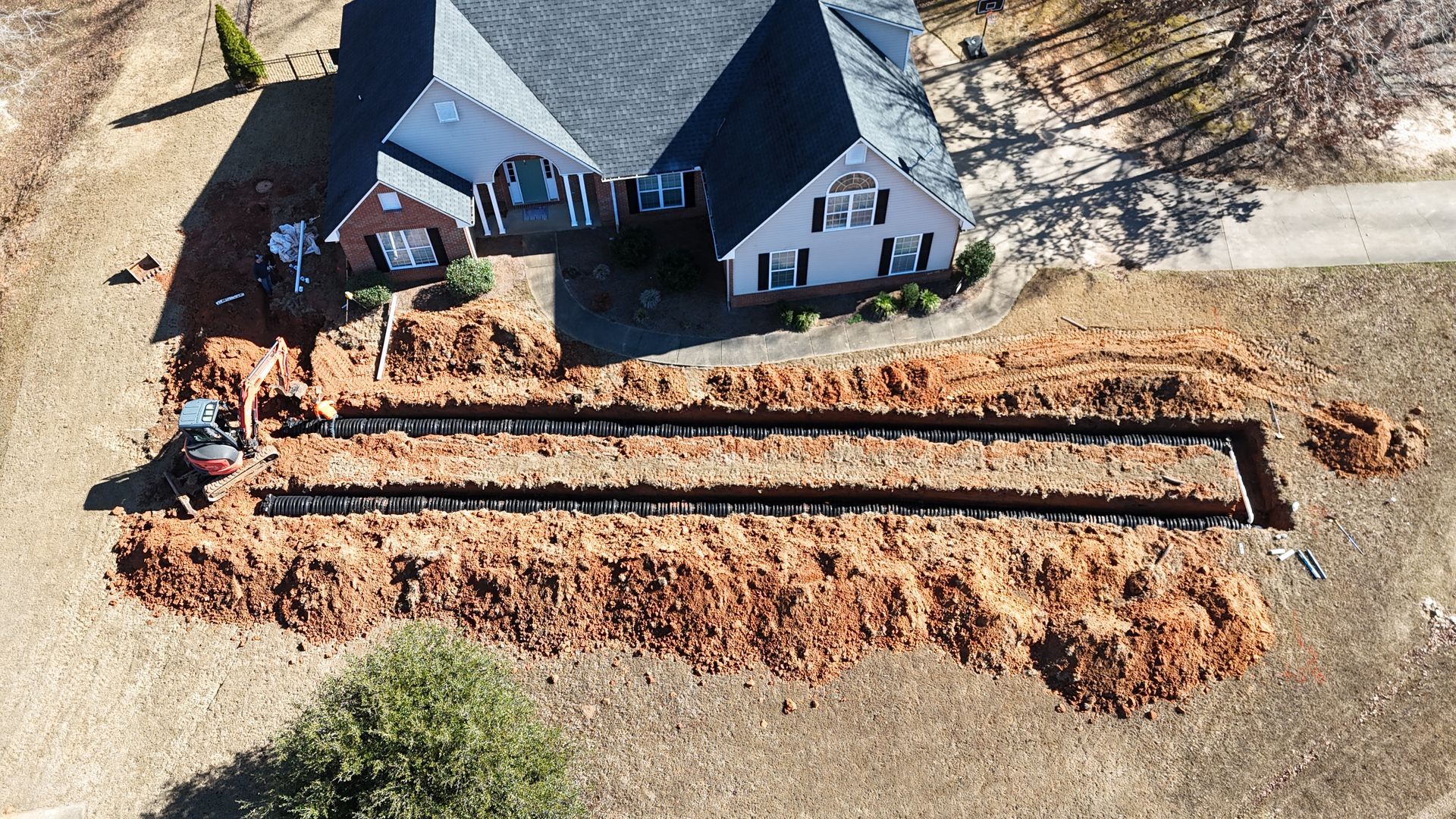 Aerial view of a house with a long excavated trench and dirt piled along the driveway.
