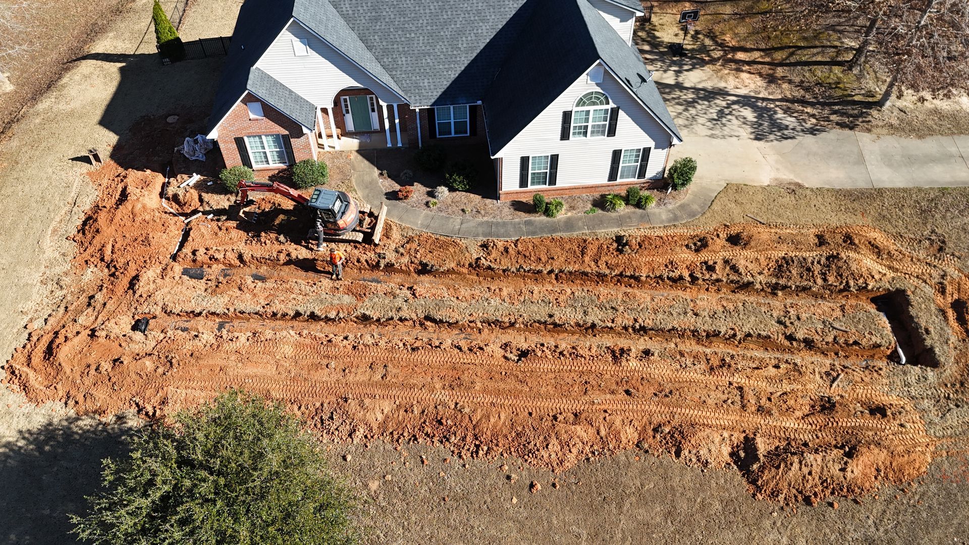 Aerial view of a house with a large dirt excavation trench along the front yard.