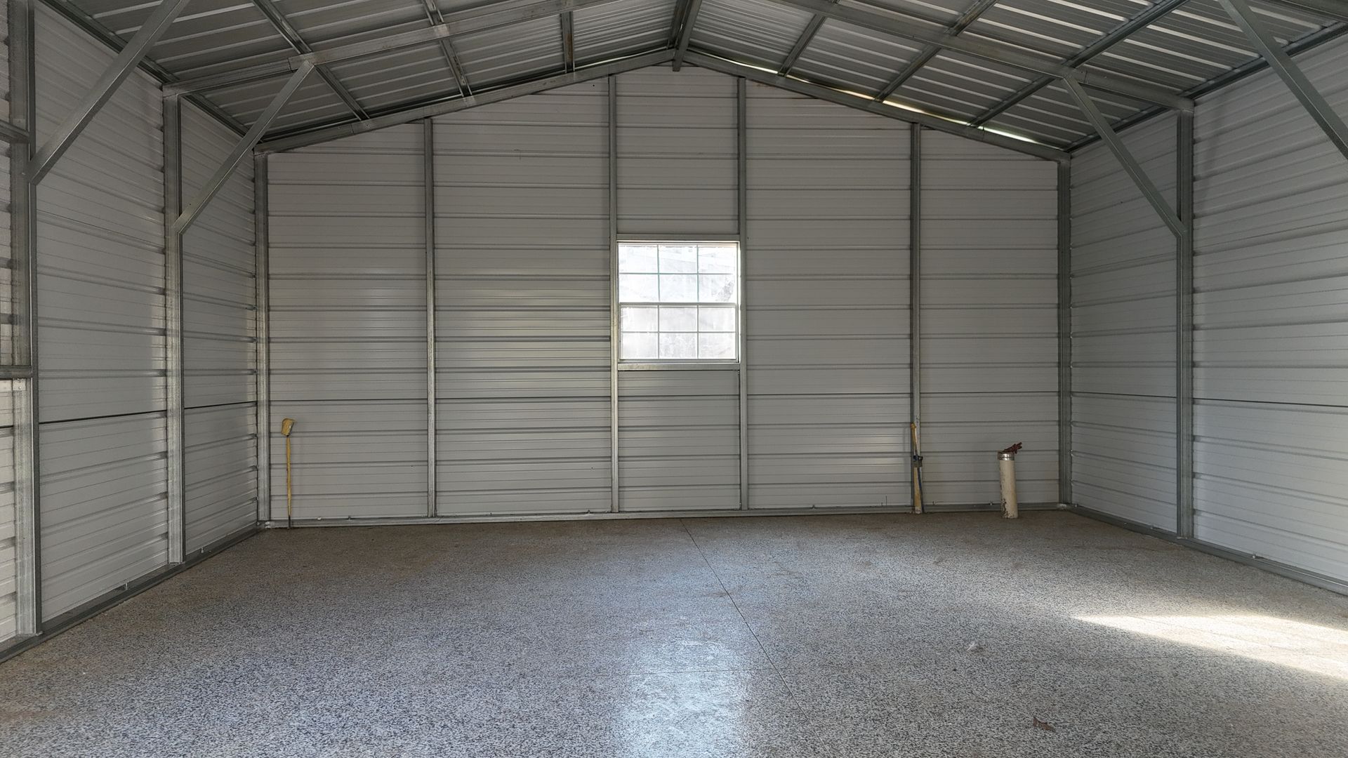 Empty gray metal shed interior with window. Gravel floor, vertical metal siding.