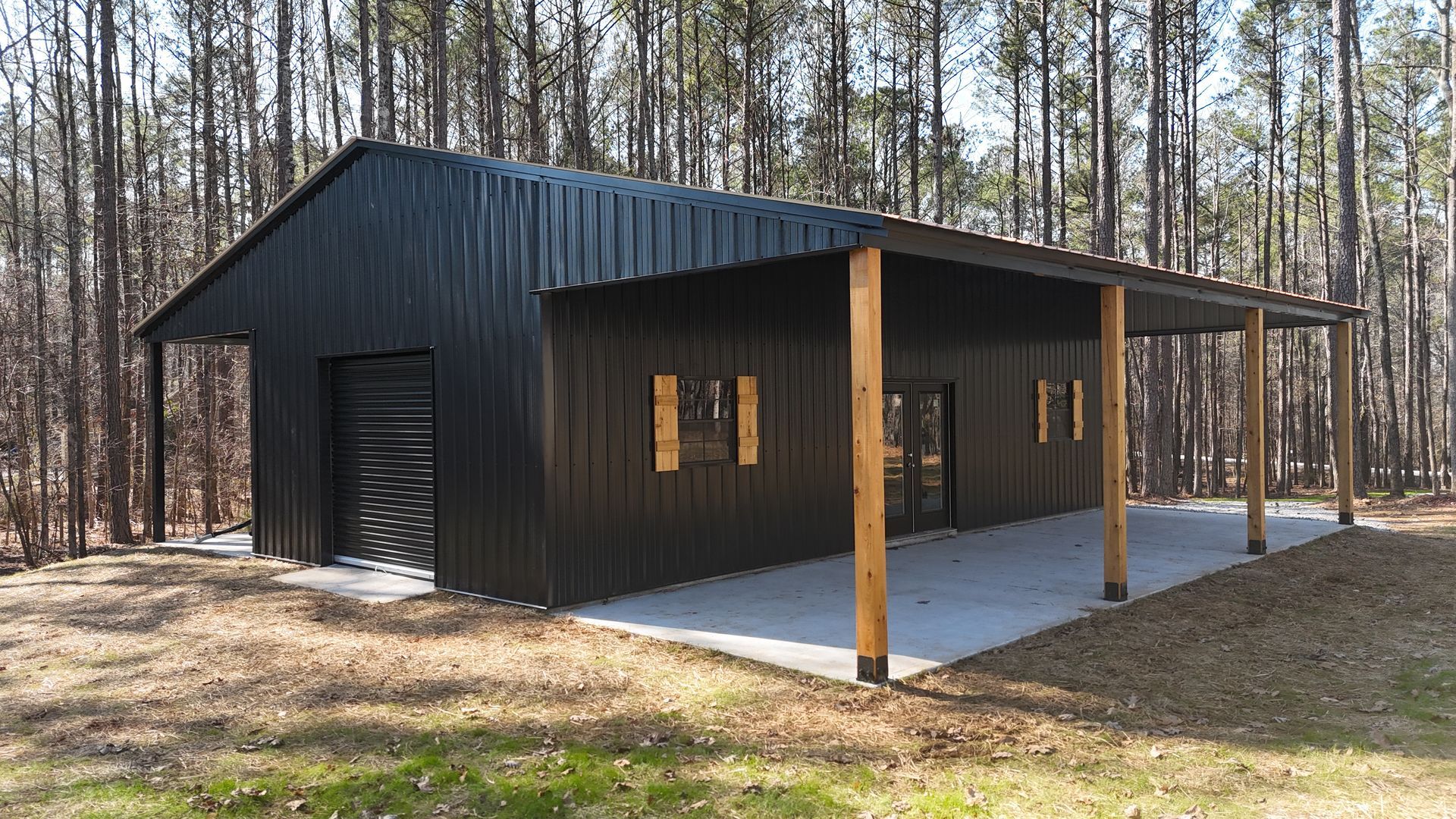 Black metal-clad building with a covered porch; set in a wooded area.