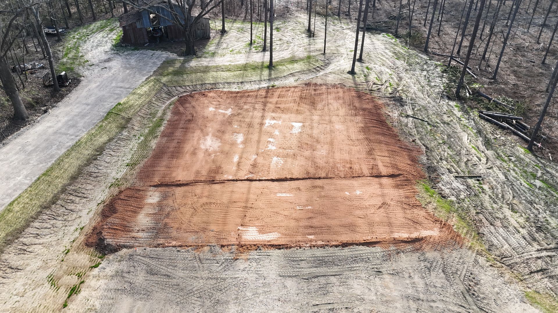 Aerial view of an empty rectangular clay court surrounded by gravel and trees