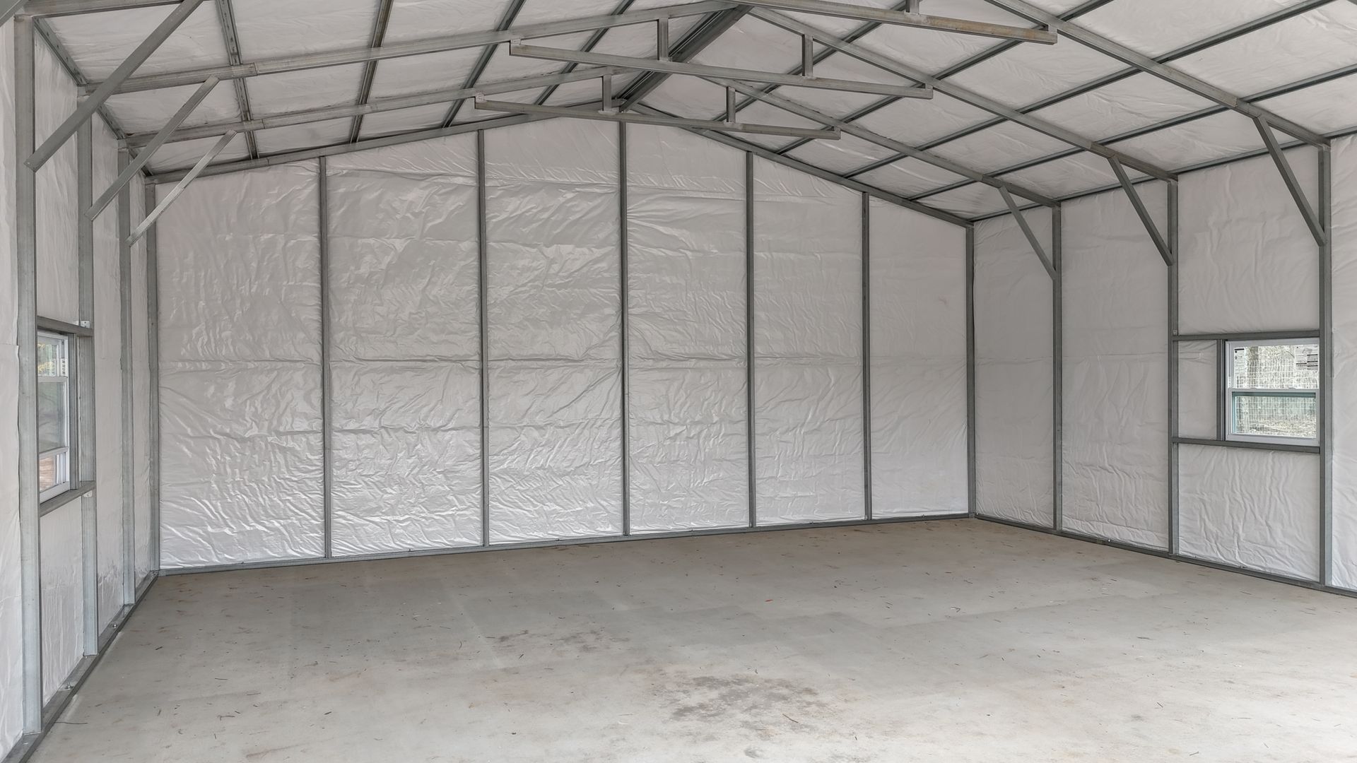 Empty metal-framed shed interior with a concrete floor and a small window on the right