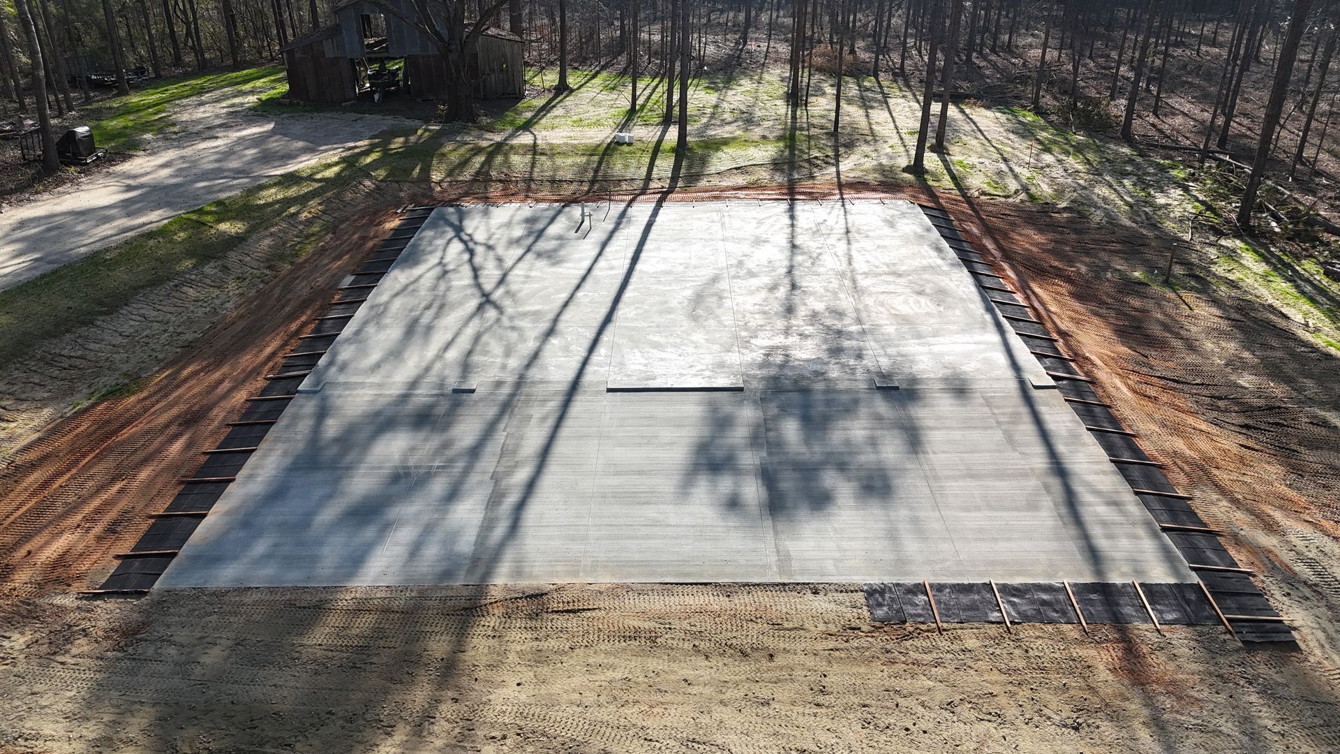 Concrete foundation slab in a wooded lot, with a rectangular opening near the center.