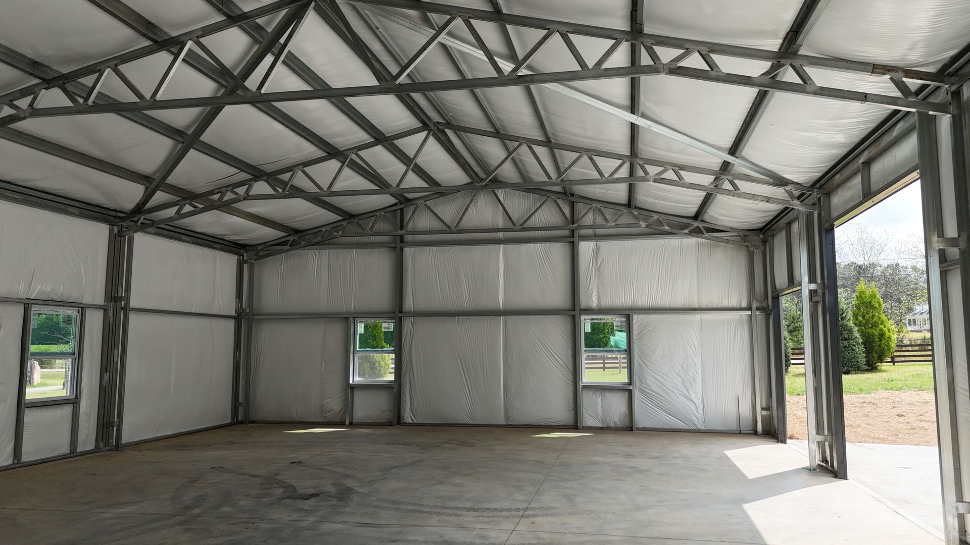 Empty industrial warehouse interior with metal trusses, gray walls, and concrete floor, sunlight through open doorway
