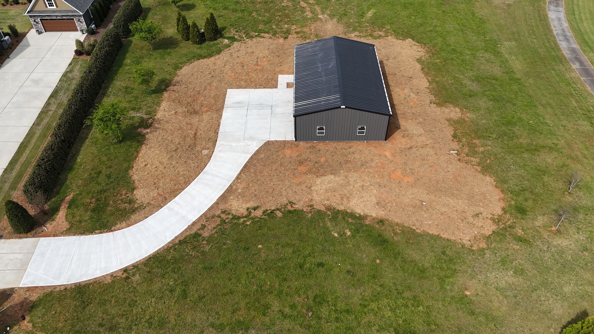 Aerial view of a small gray shed with a curved white walkway in a grassy yard.
