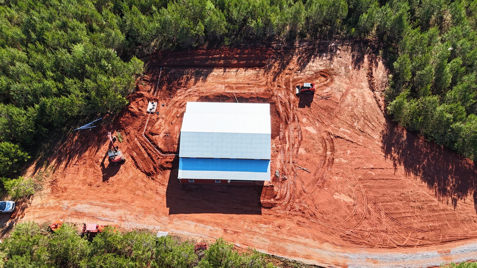 A small building with a blue roof on a cleared red dirt hillside surrounded by dense green vegetation.