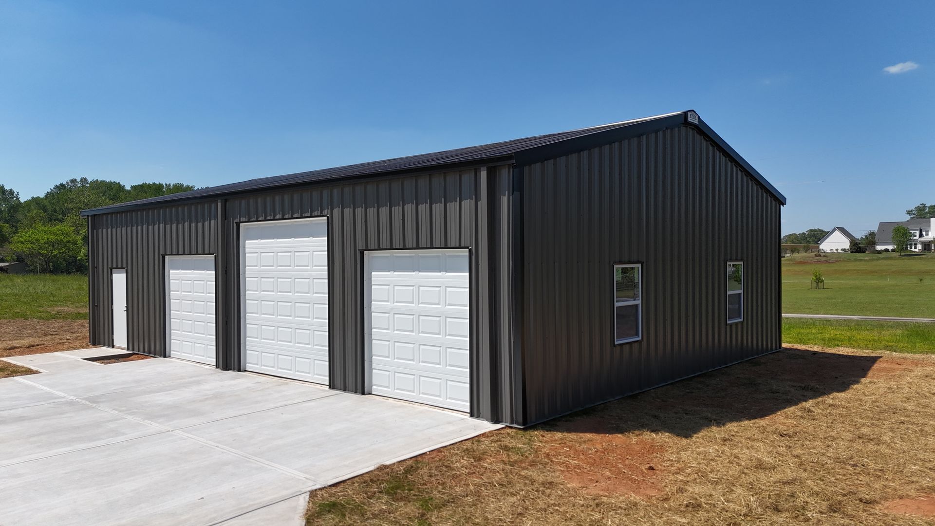 Black metal garage with three white doors beside a concrete driveway under a clear sky