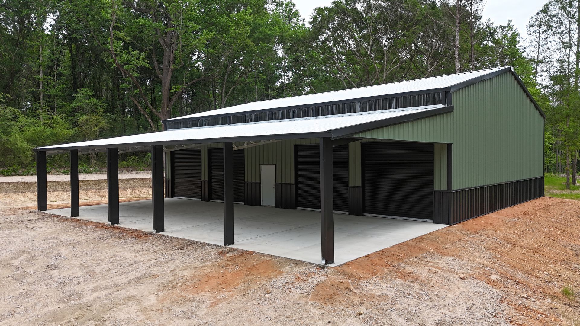 Green metal shed with a covered porch in a wooded clearing