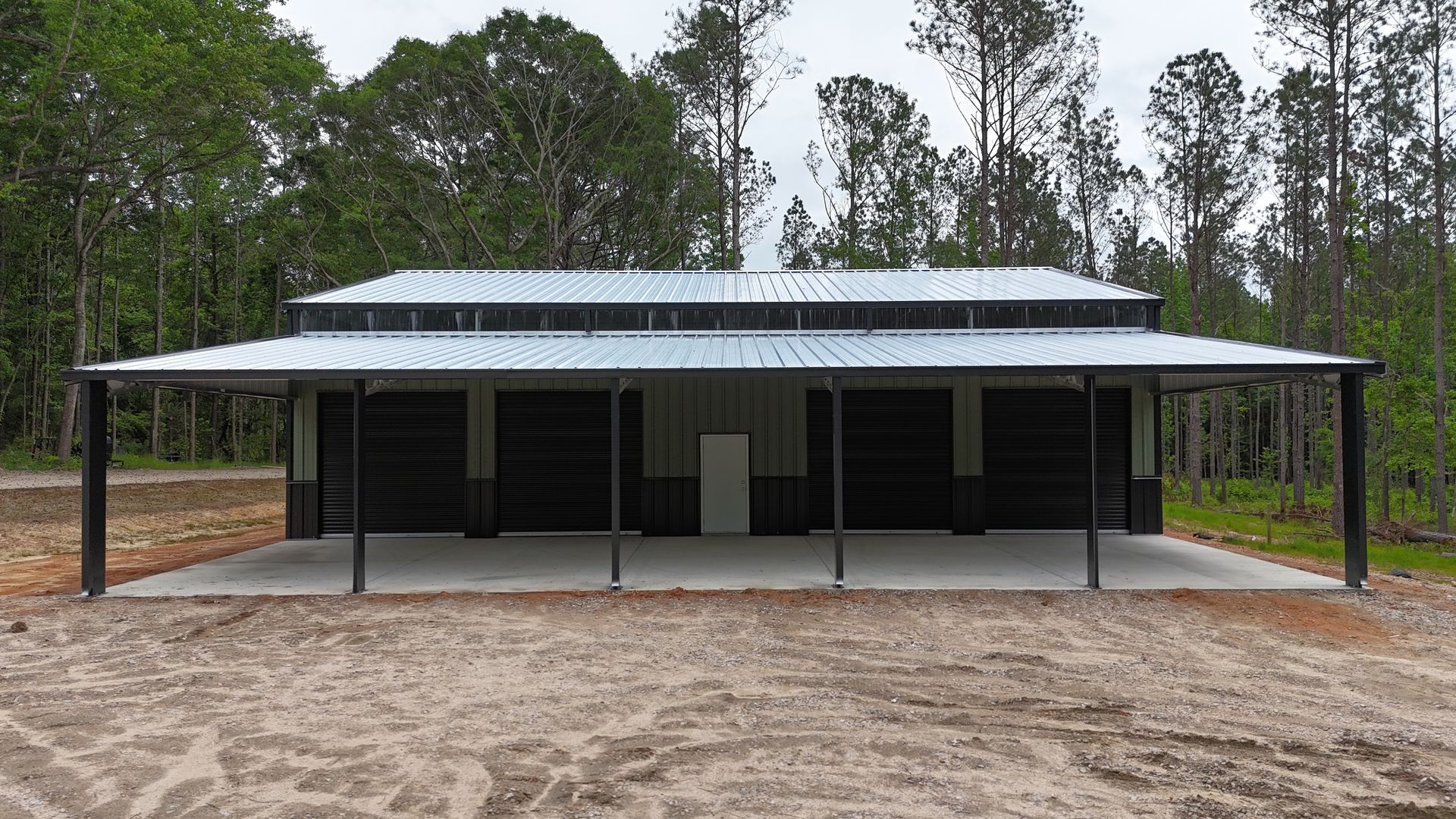 Front view of a dark metal pavilion with a concrete slab and surrounding pine trees