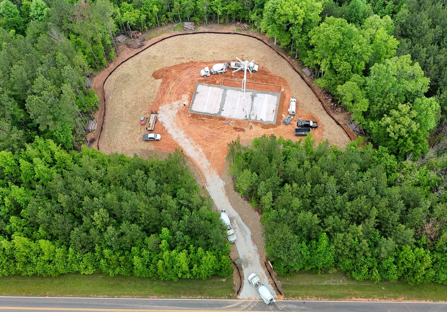 Aerial view of a small construction site with dirt clearing, equipment, and a road at the bottom edge