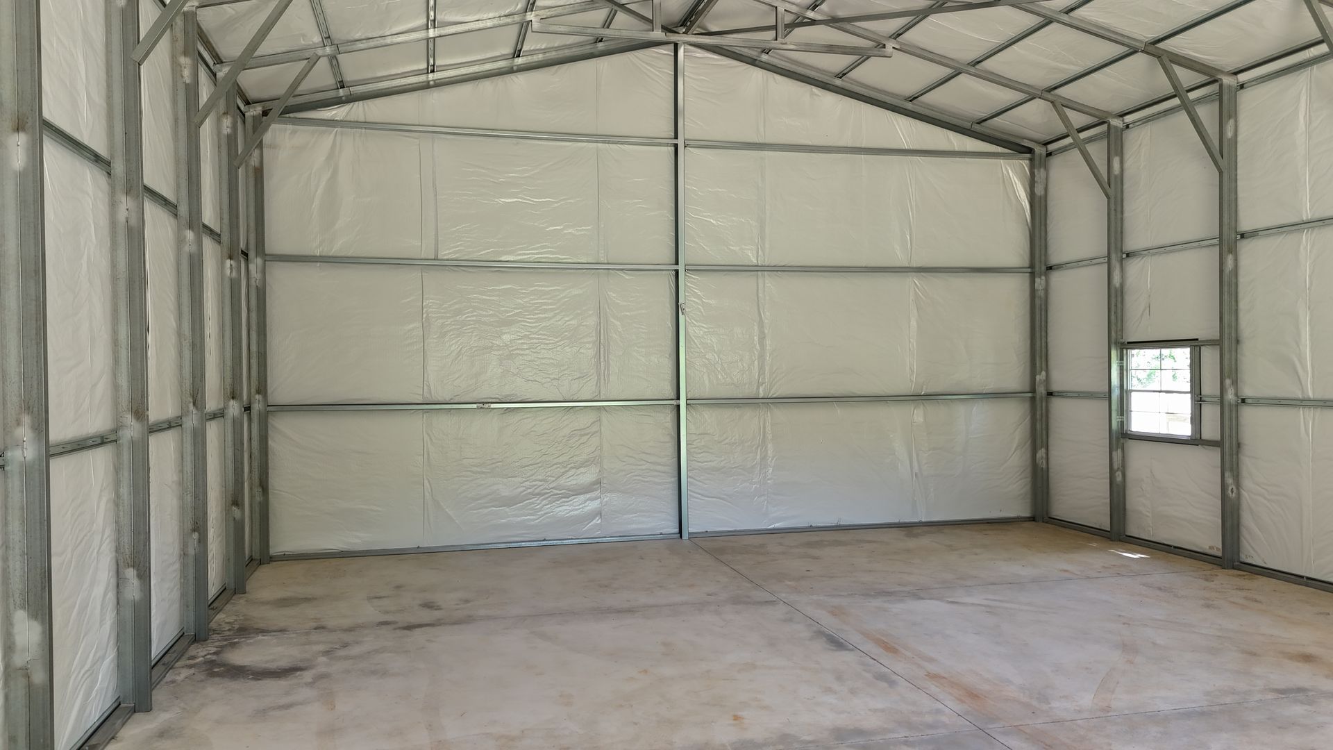 Empty metal-framed storage building interior with white insulated walls and concrete floor