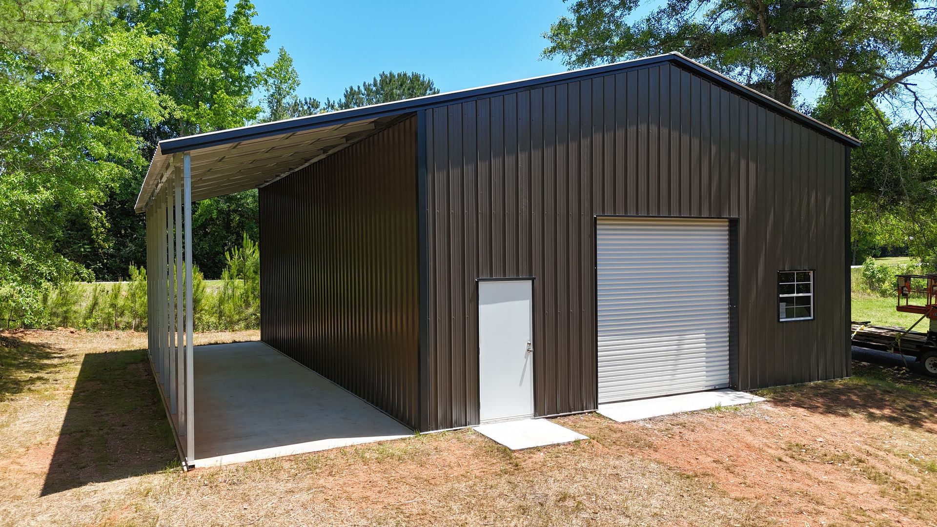 Dark metal storage shed with white roll-up door and open side bay in a wooded yard