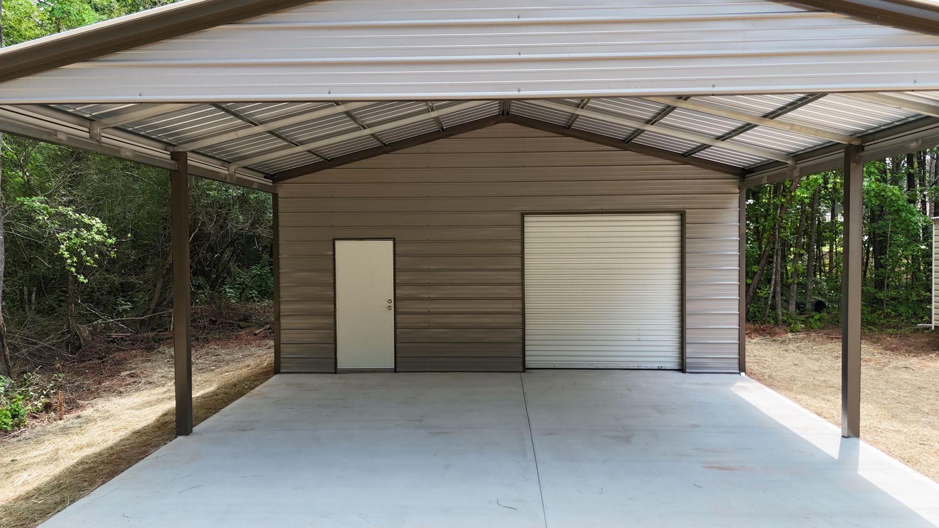 Covered concrete carport with a metal roof and a small tan storage building at the back.