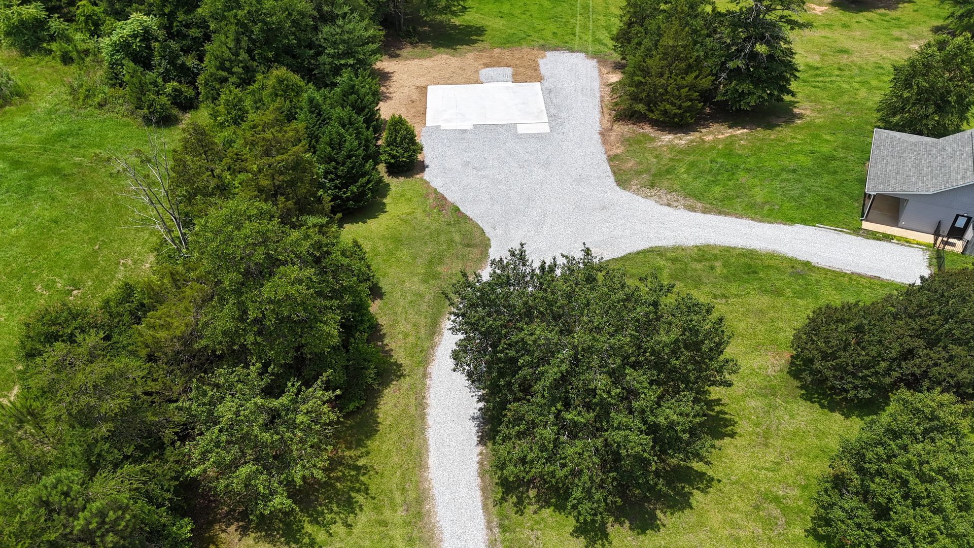 Aerial view of a gravel driveway through green trees leading to a small house and parking area.