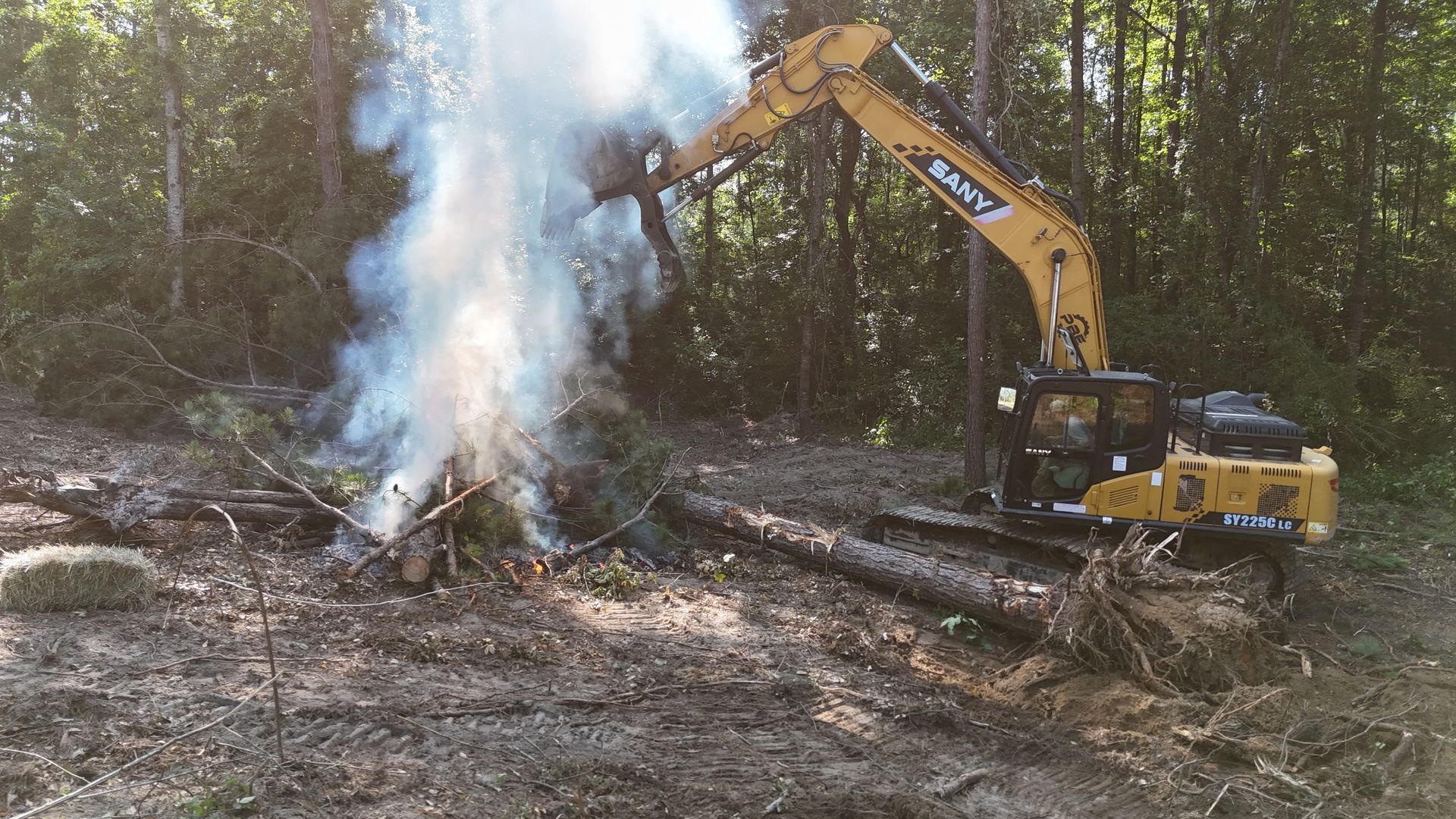 Excavator spraying water on a smoky forest fire near a log in a wooded area