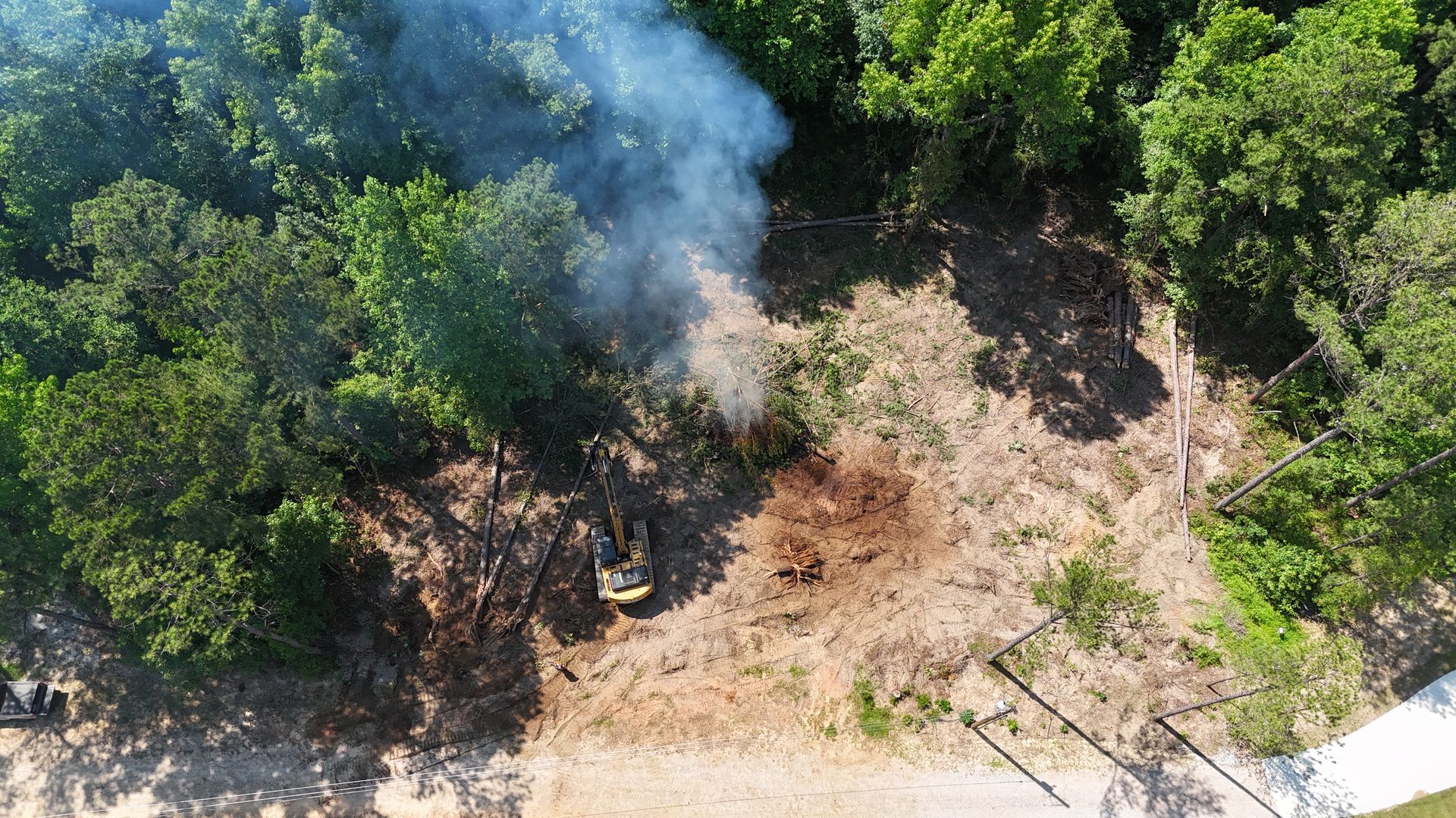 Smoke rising from a small forest fire beside a dirt road, with green trees nearby.