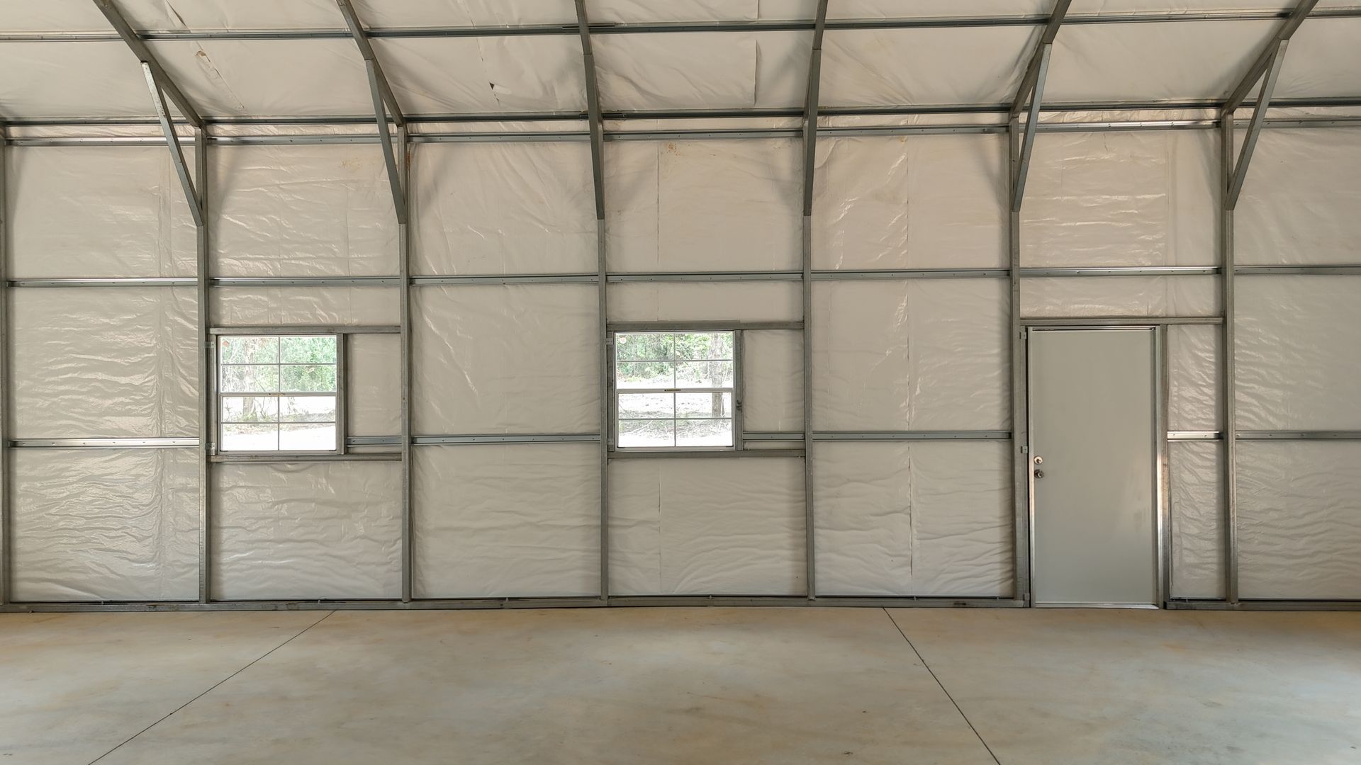 Empty industrial warehouse interior with metal wall panels, two windows, and a concrete floor