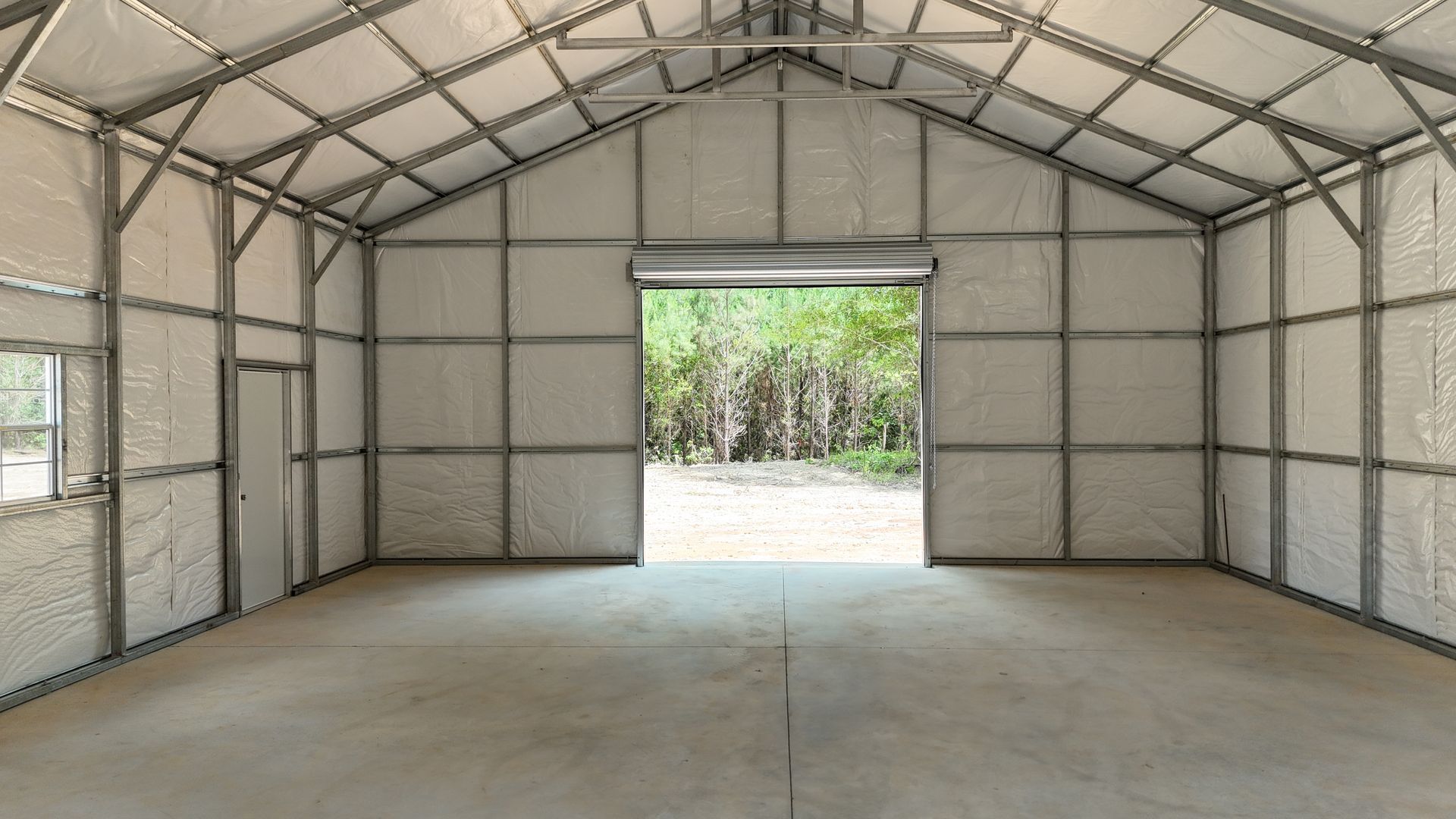 Empty metal-framed storage shed with concrete floor and open doorway to trees outside