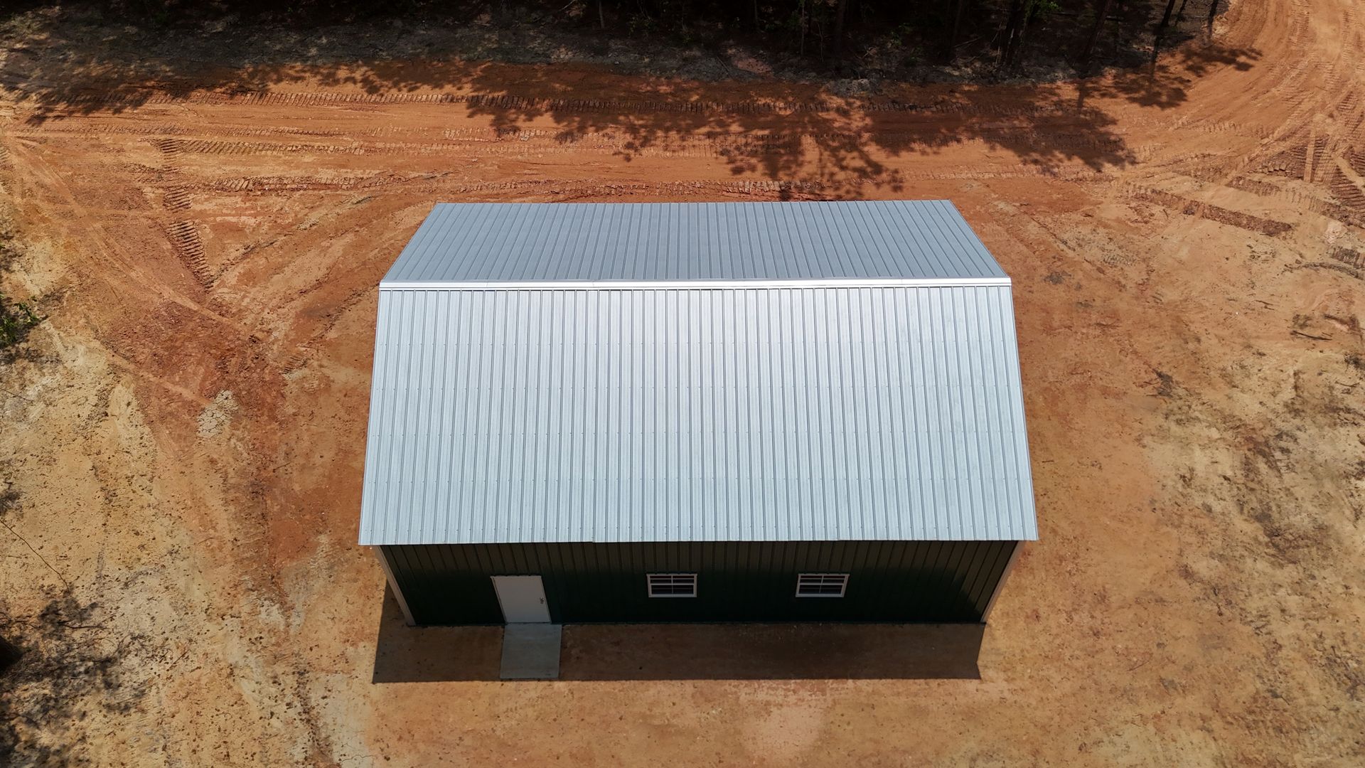 A small corrugated metal shed with a gray roof sits on reddish dirt, viewed from above.