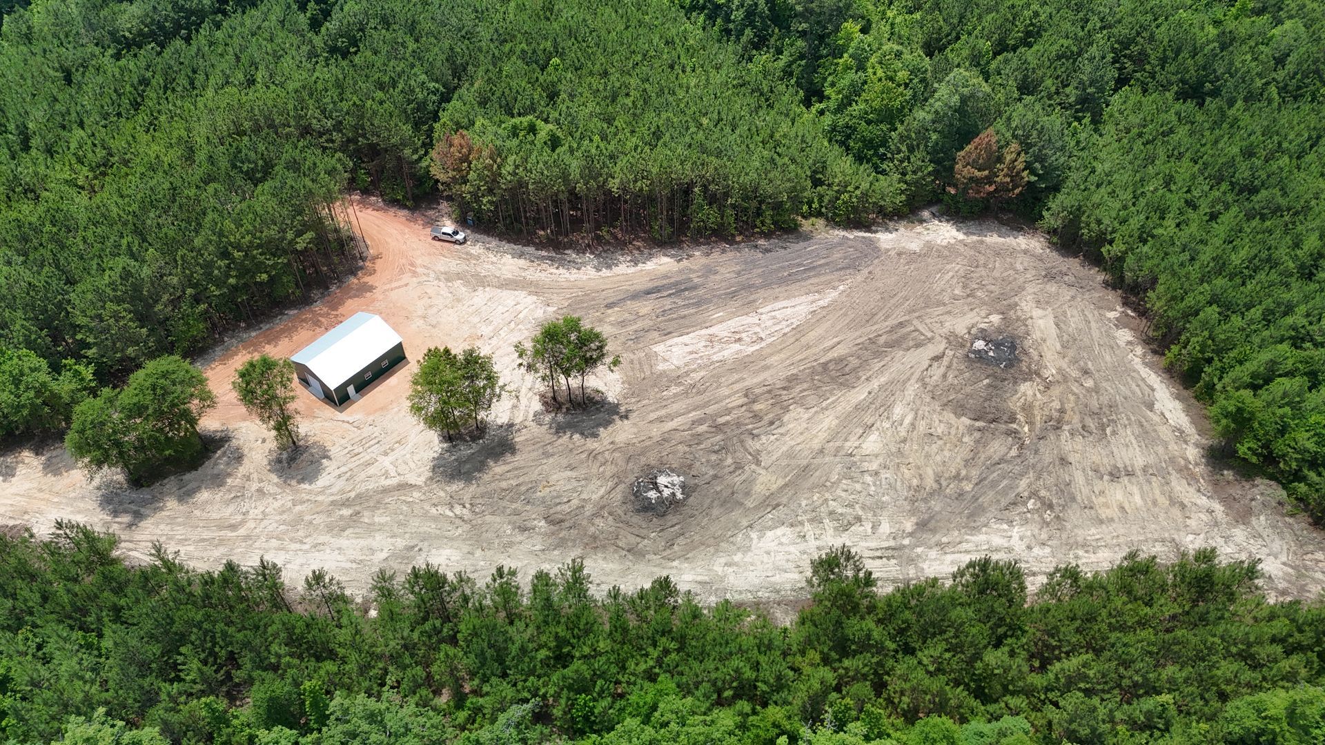 Aerial view of a dirt clearing surrounded by dense green forest with a small white shelter