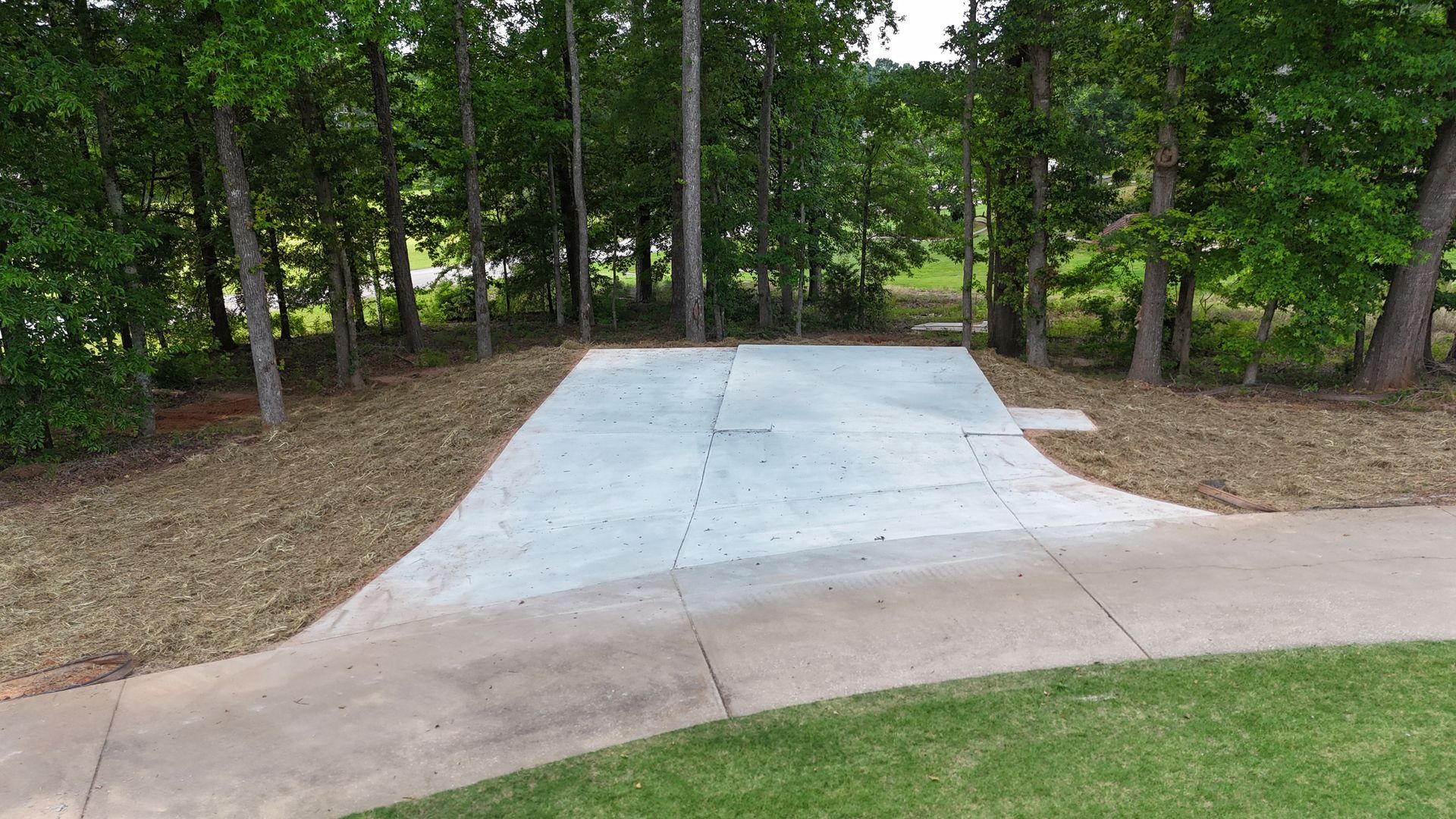 Concrete driveway leading into a wooded area with trees on both sides.