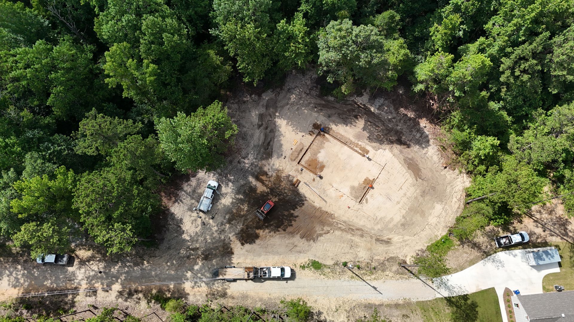 Aerial view of a forest clearing with a dirt construction site and vehicles along the road.