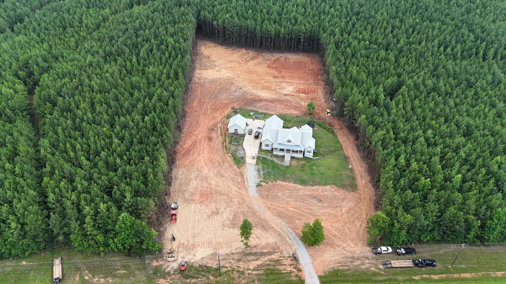 Aerial view of a white house in a clearing surrounded by dense green forest and dirt roads